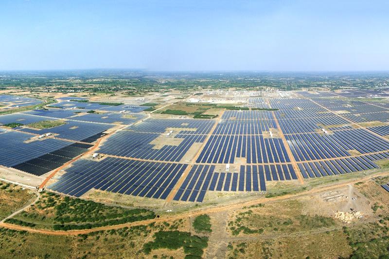 Aerial view of Kamuthi Solar Park with rows of solar panels spread across a large area of land under a clear sky.